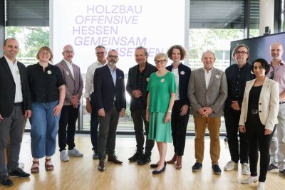 Zweites Netzwerktreffen Eine Gruppe von Personen vor einem Leuchtschild mit dem Slogan "Holzbauoffensive Hessen gemeinsam umsetzen"