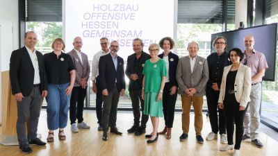 Zweites Netzwerktreffen Eine Gruppe von Personen vor einem Leuchtschild mit dem Slogan "Holzbauoffensive Hessen gemeinsam umsetzen"